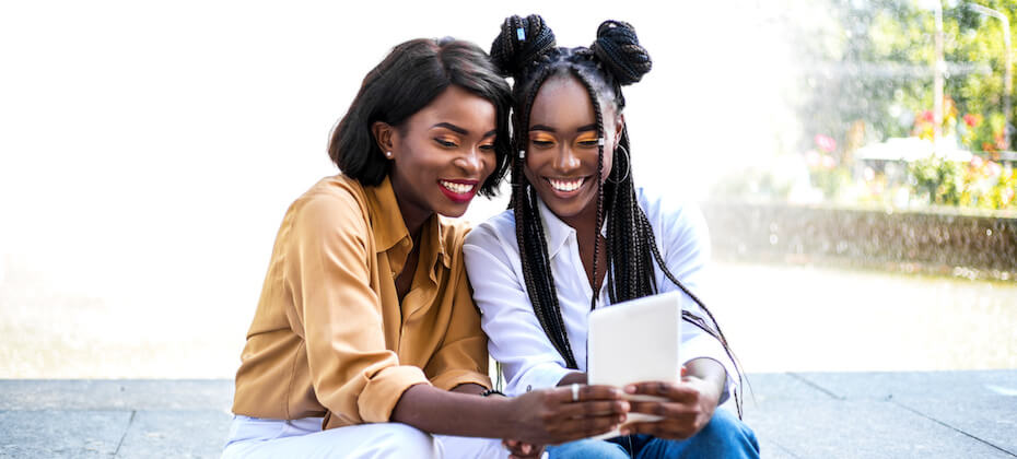 Two friends look at a tablet device. 