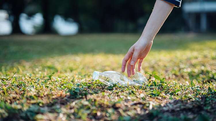 A person picks up a discarded plastic bottle, for recycling.